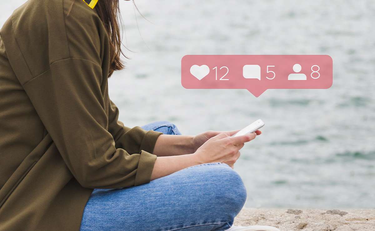 Persona seduta vicino all’acqua mentre guarda lo smartphone con notifiche social