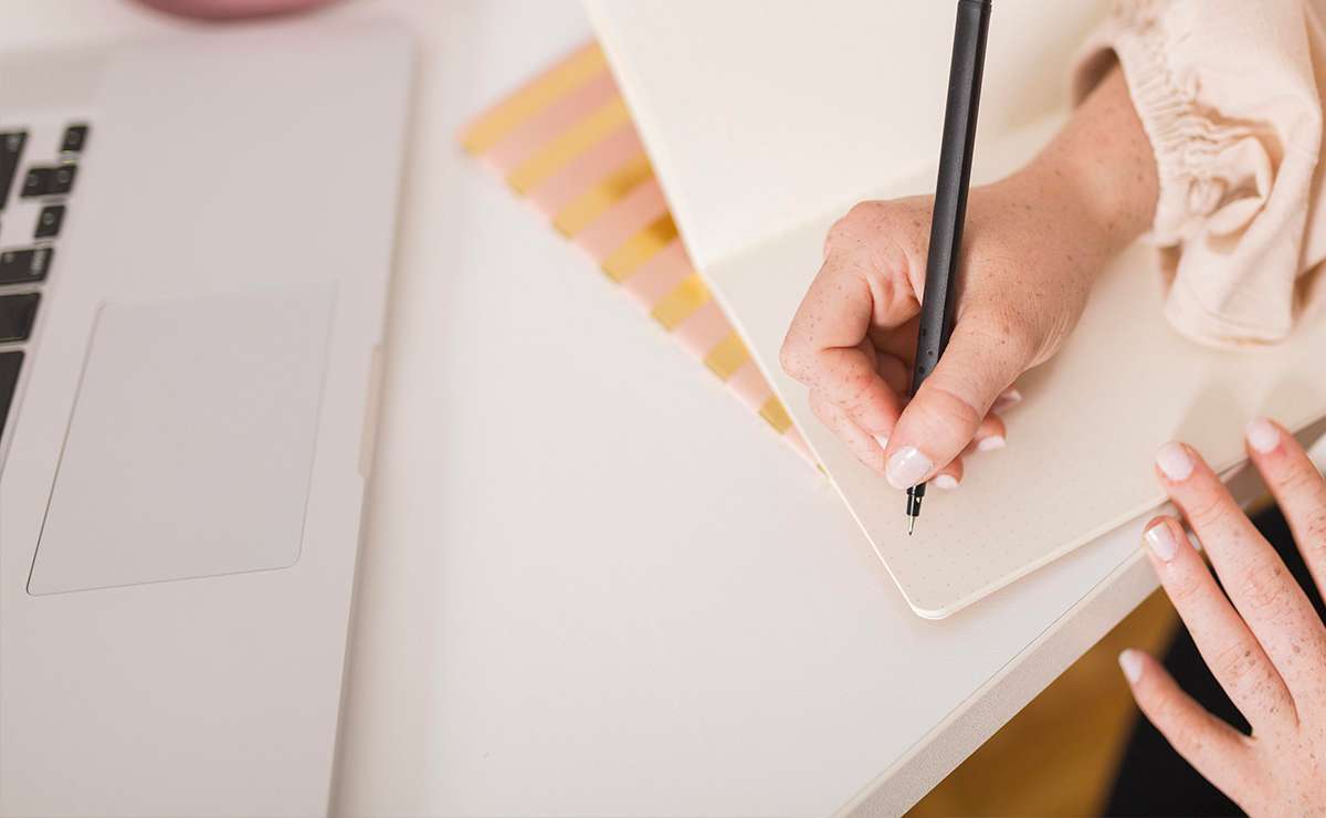 Mano che scrive su un quaderno accanto a un laptop