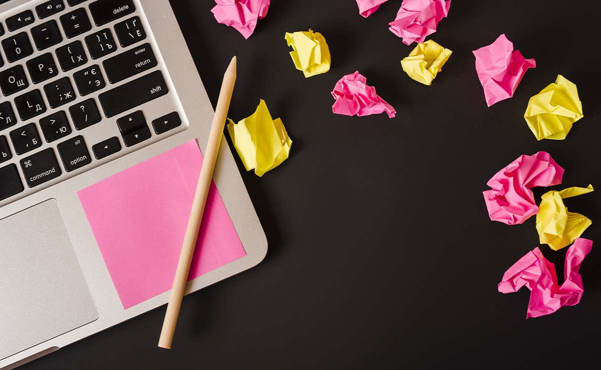 Computer portatile con tastiera visibile, matita e post-it rosa su una scrivania nera
